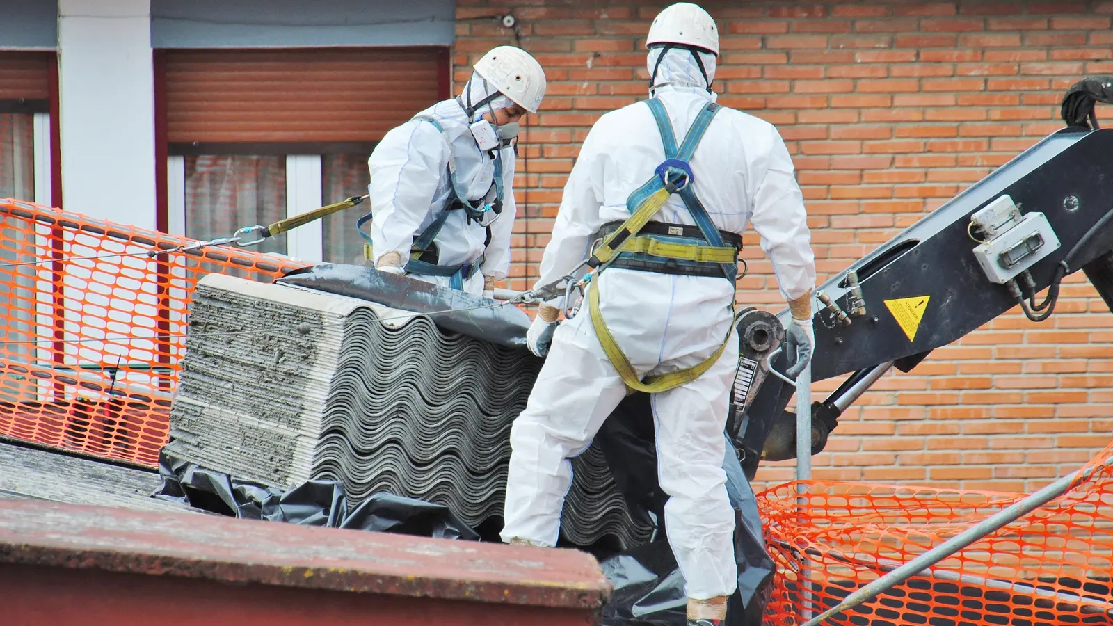 Asbestos removal team lifting cement roofing sheets by crane at a commercial building